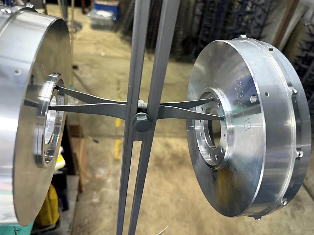 Two large aluminum discs for tobacco automation equipment hung on a rack for hard anodizing