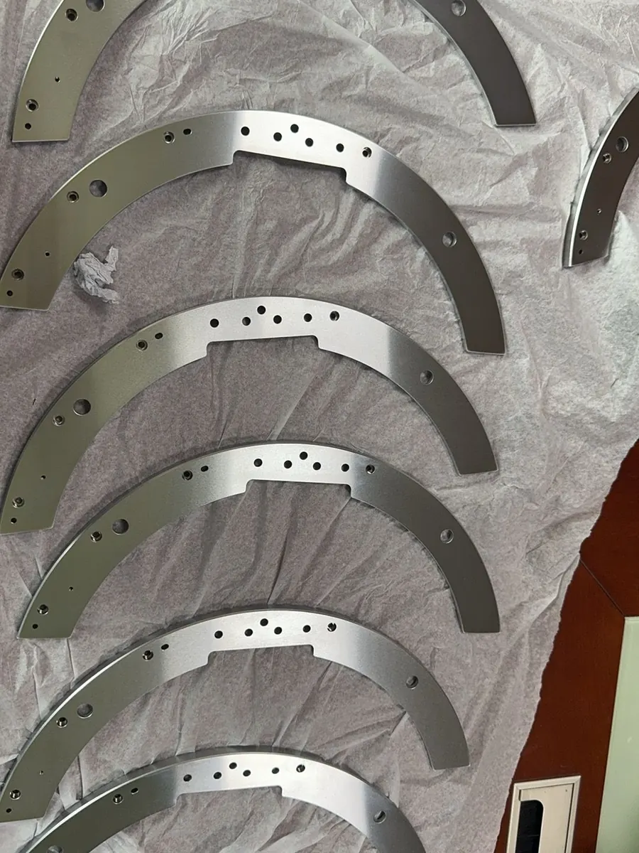 A small batch of CNC machined aluminum arc plates with drilled and tapped holes, laid out after machining